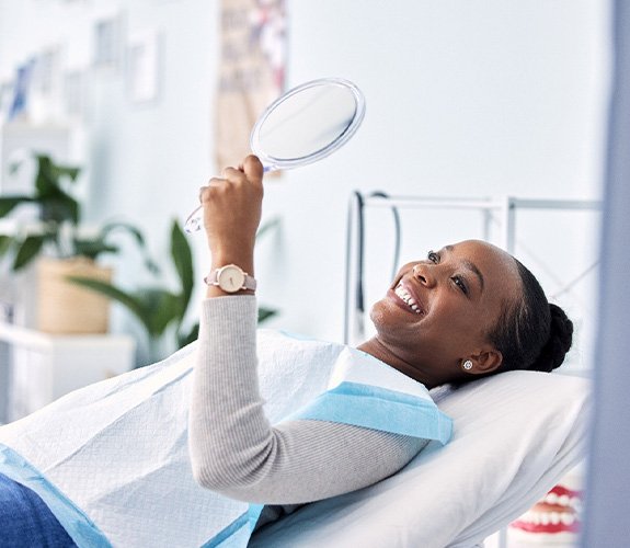 Woman smiling at reflection in handheld mirror