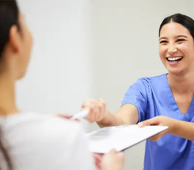Dental assistant smiling while handing patient forms