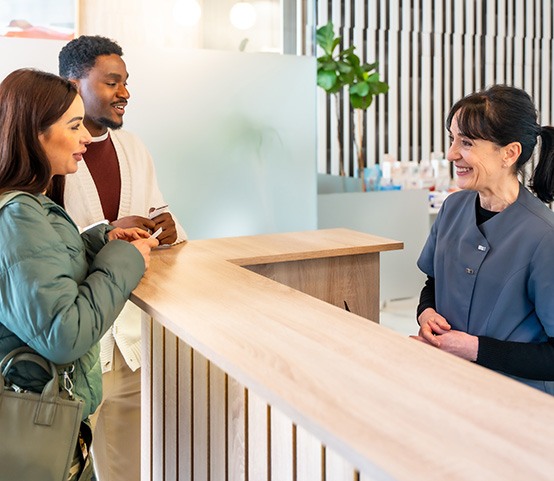 Happy couple talking to dental receptionist about dental insurance