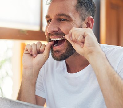 Man smiling while flossing teeth in bathroom