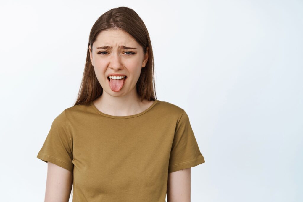 Woman in brown shirt sticking tongue out from bad taste in mouth