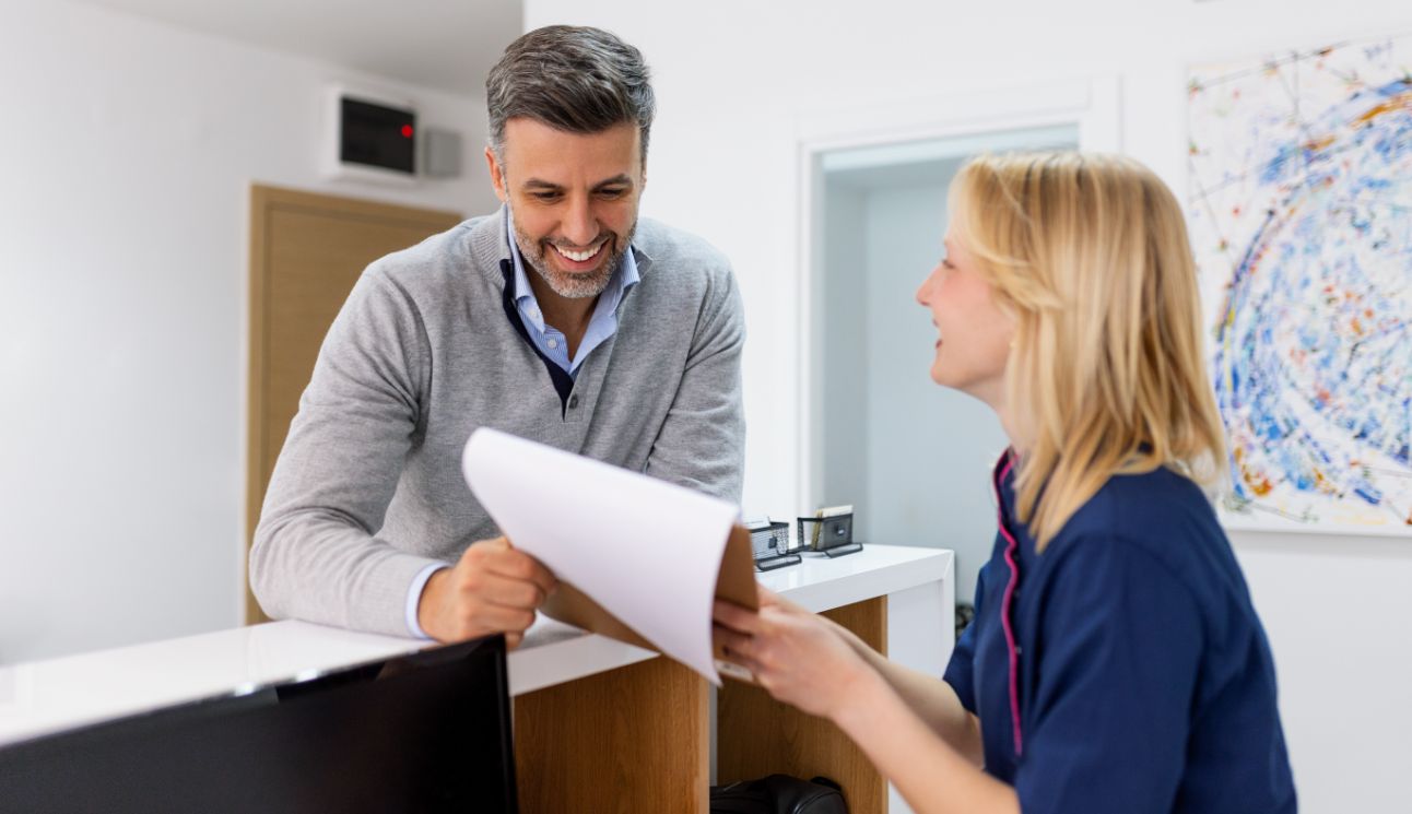 Dental team member at front desk handing a clipboard to a patient